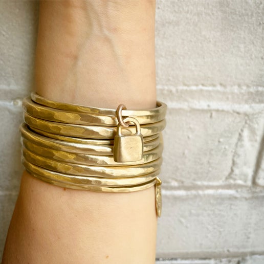 Stack of gold bangles, one with a lock charm, on a wrist against a light background