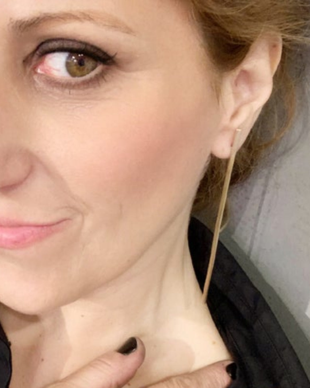 Close-up of a woman wearing a gold bar earring with a blurred background