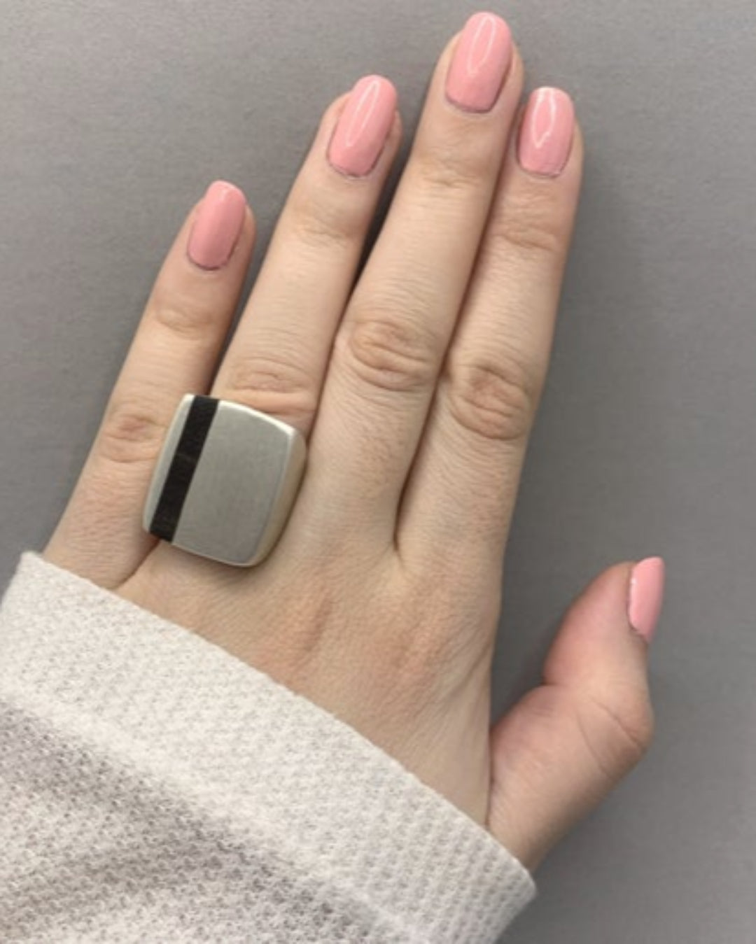 Hand wearing a silver ring with wooden inlay against a grey background