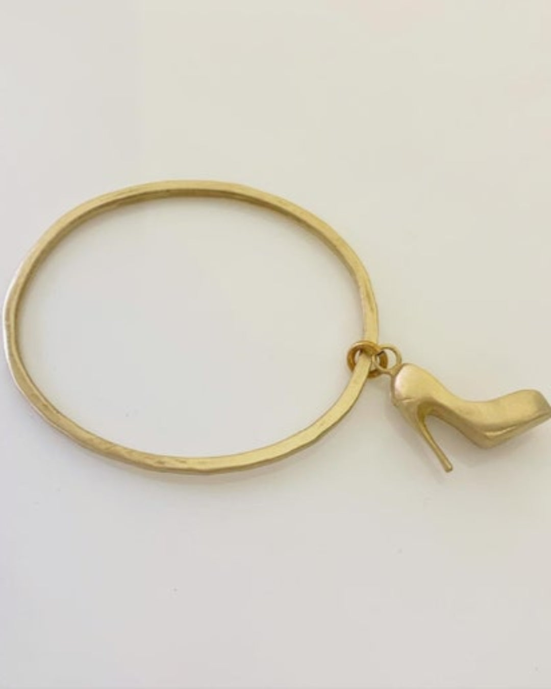 Gold bangle with a high-heeled shoe charm on a light gray background