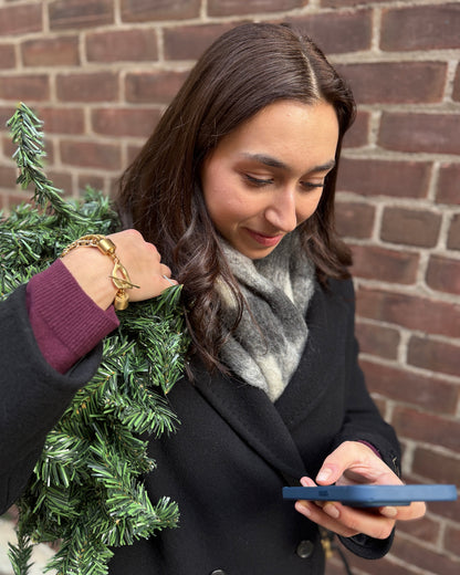 Woman holding a smartphone and a small Christmas tree against a brick wall.