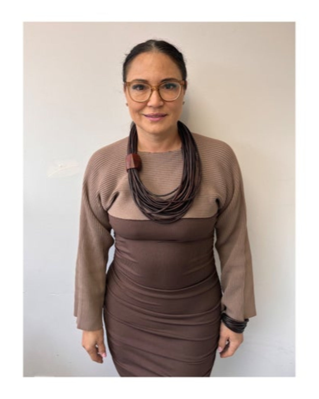 Woman wearing a brown dress and multistrand brown leather necklace with wooden detail on a plain background