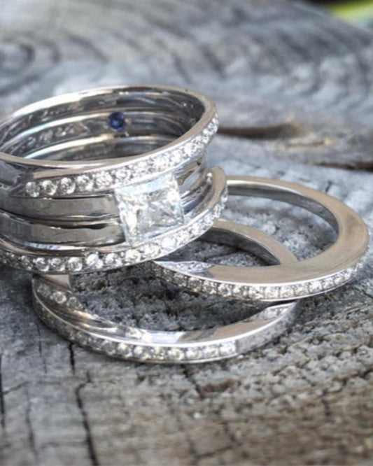 Stack of diamond rings. Two diamond bands and a ring featuring two diamond bands and one large diamond on a textured surface