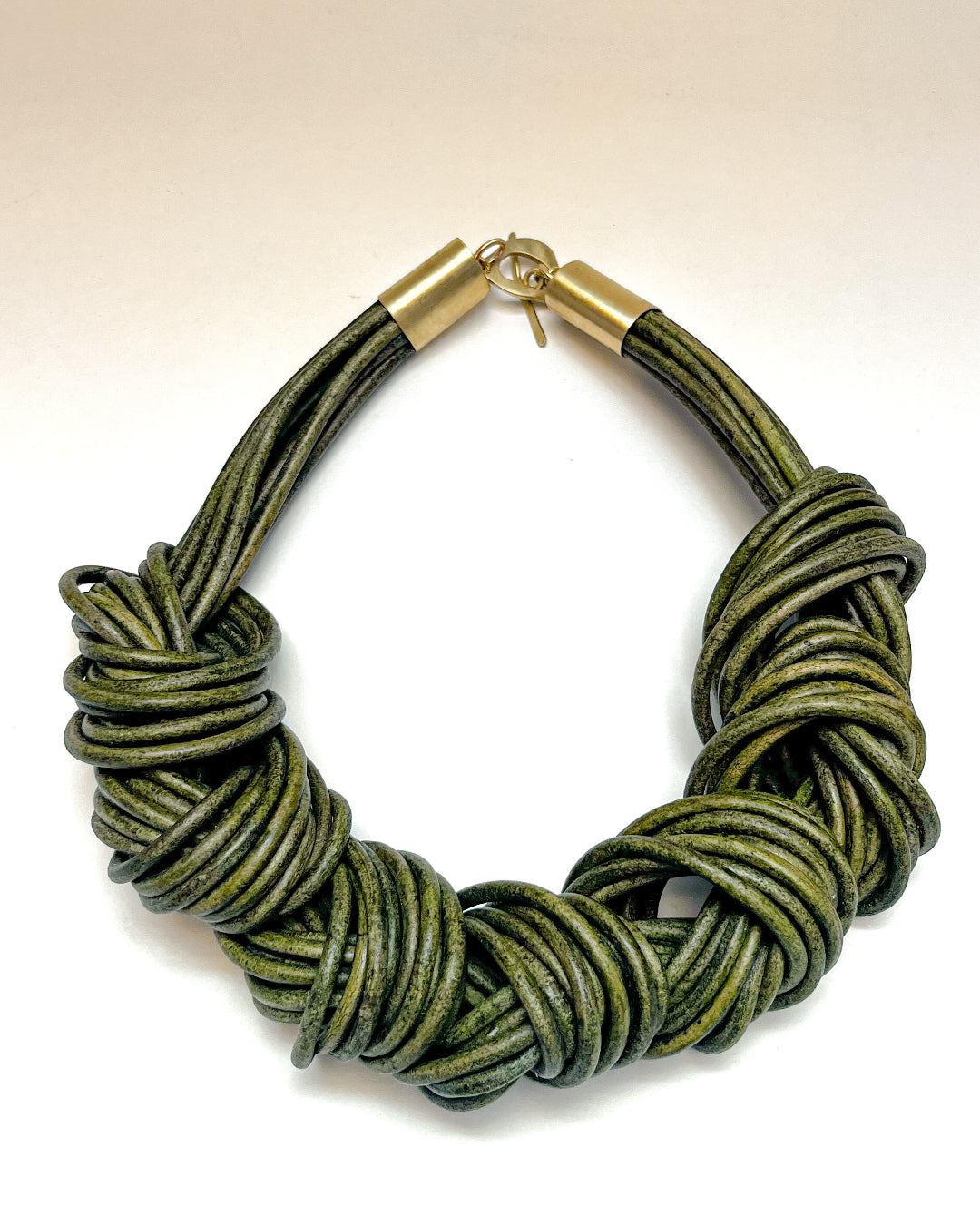 Green multistrand leather knotted necklace with a gold clasp on a white background