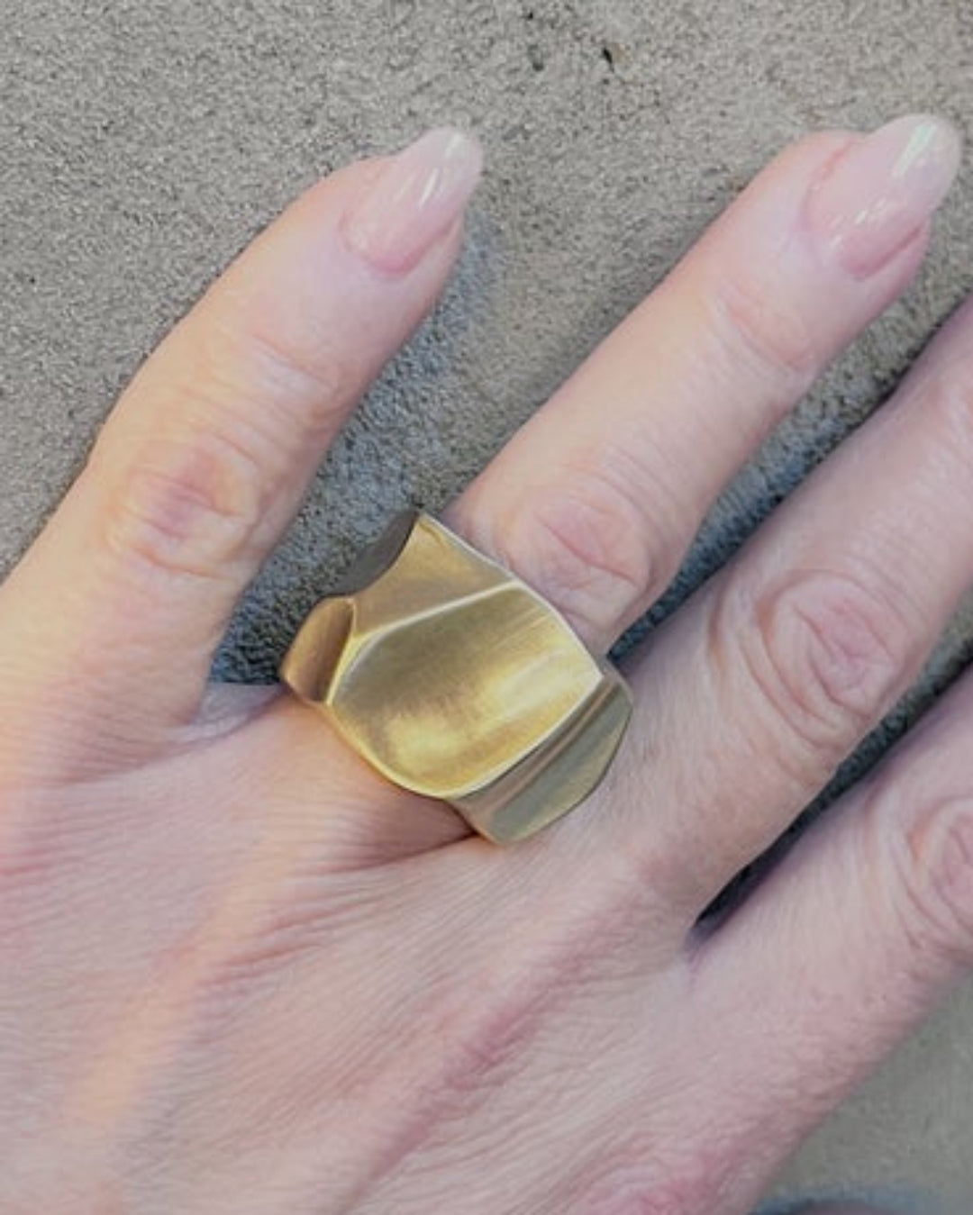 Textured gold ring on a hand with a concrete background