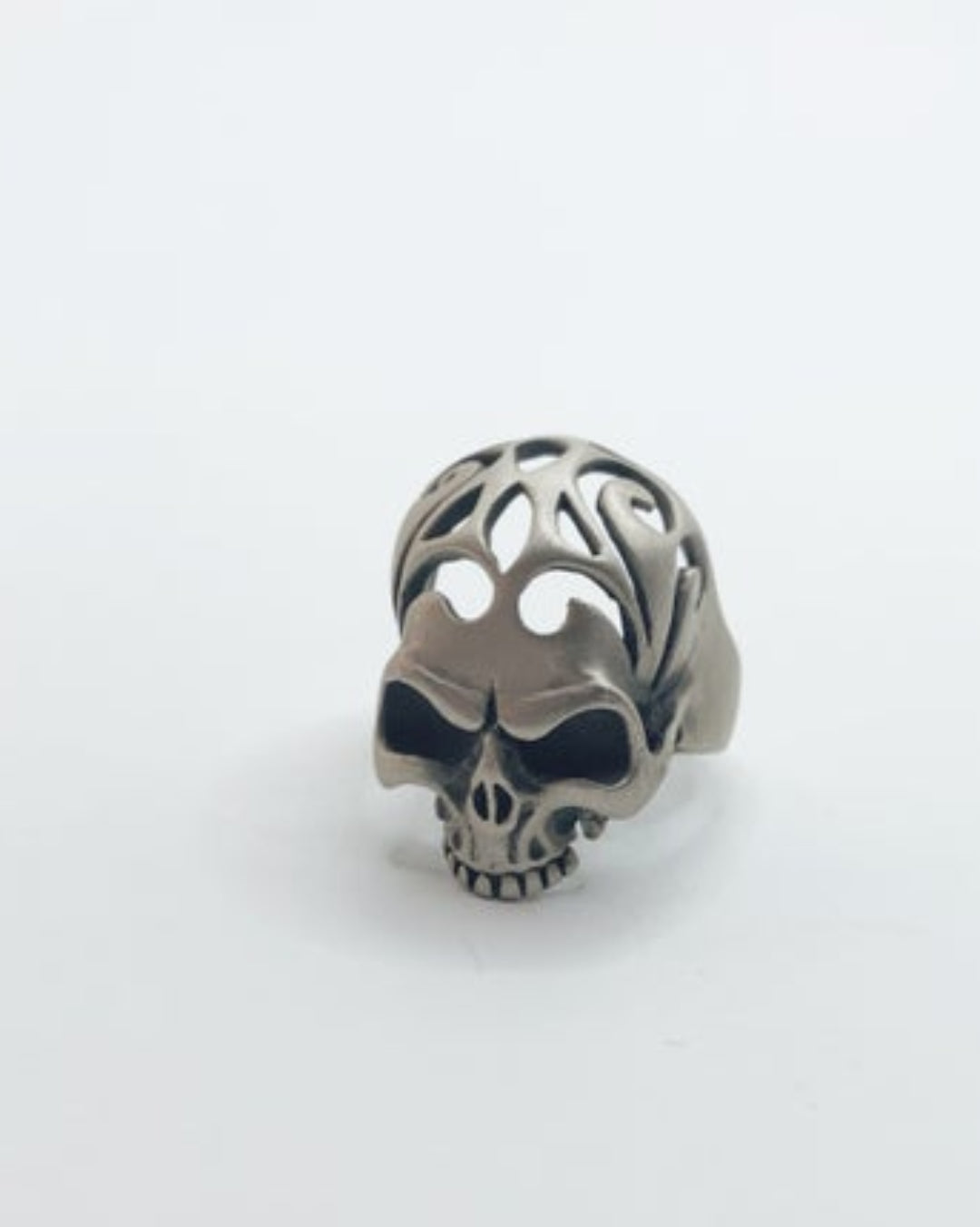 Silver skull-shaped ring with intricate design on a white background
