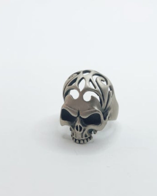 Silver skull-shaped ring with intricate design on a white background
