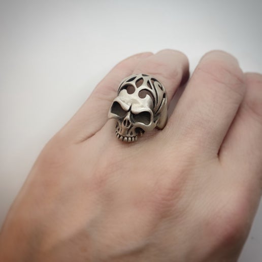 Skull-shaped ring with cutout details on a person's finger against a plain background