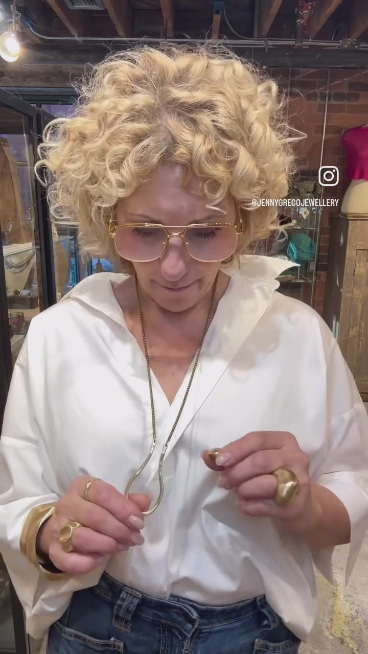Woman in a white shirt wearing bold gold jewellery in a retail store setting