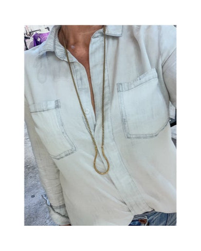 Person wearing a light-coloured shirt with a long bronze necklace 