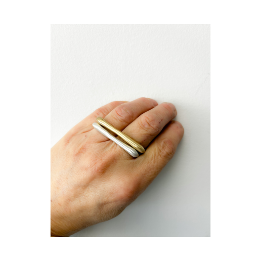 Hand wearing two rings, one gold and one silver, on a white background