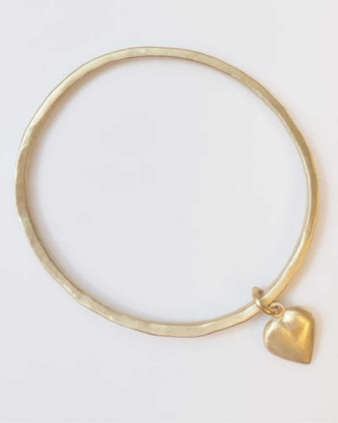 Gold bangle with a heart charm on a white background