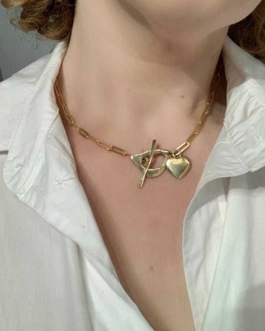 Gold necklace with heart pendant worn by a person in a white shirt.
