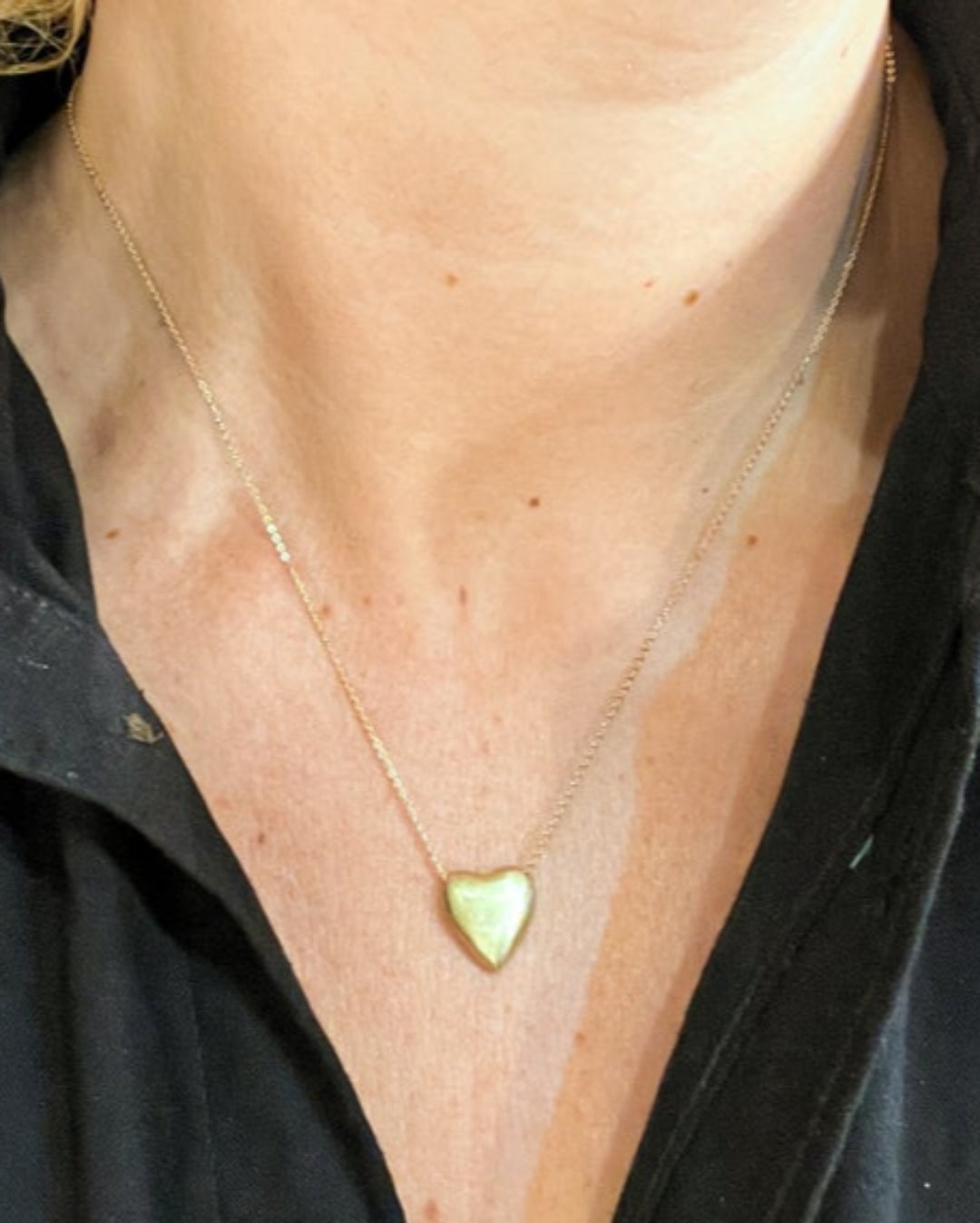Gold necklace with a heart-shaped pendant on a person wearing a black garment.