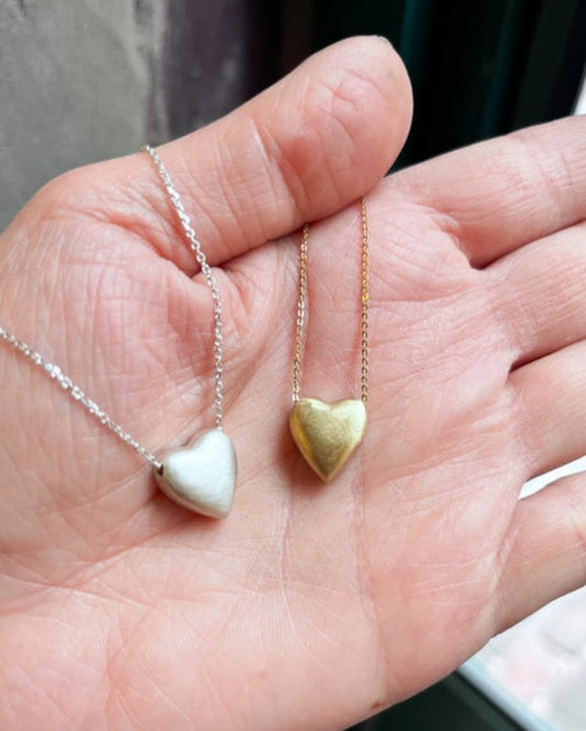 Two necklaces with heart-shaped pendants, one gold and one silver, held in a hand.