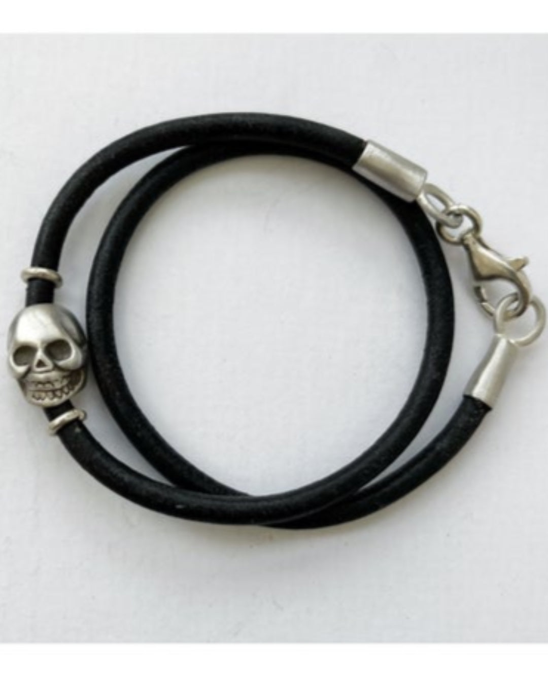 Black double wrap leather bracelet with silver skull charm on a white background