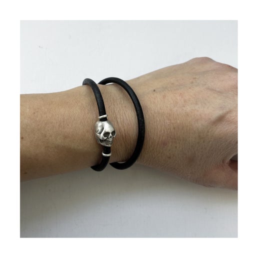 Black double wrap leather bracelet with a silver skull charm on a wrist against a white background