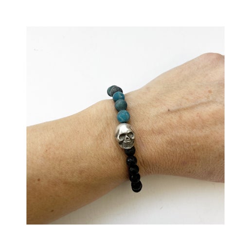 Beaded bracelet with black and blue beads and a silver skull charm on a wrist against a white background