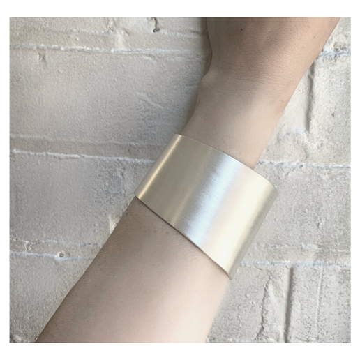 Silver cuff on a person's wrist against a light stone wall background