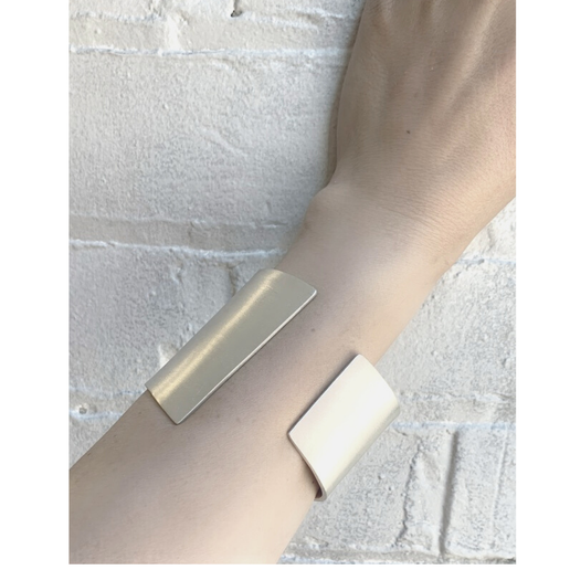 Metallic cuff with geometric design on a person's wrist against a light stone wall background