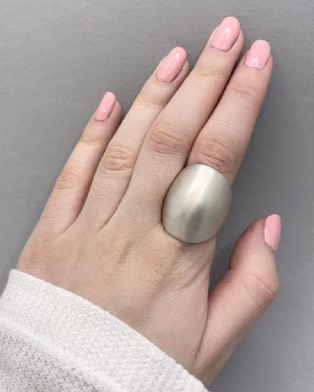 Hand wearing a large silver ring on a grey background