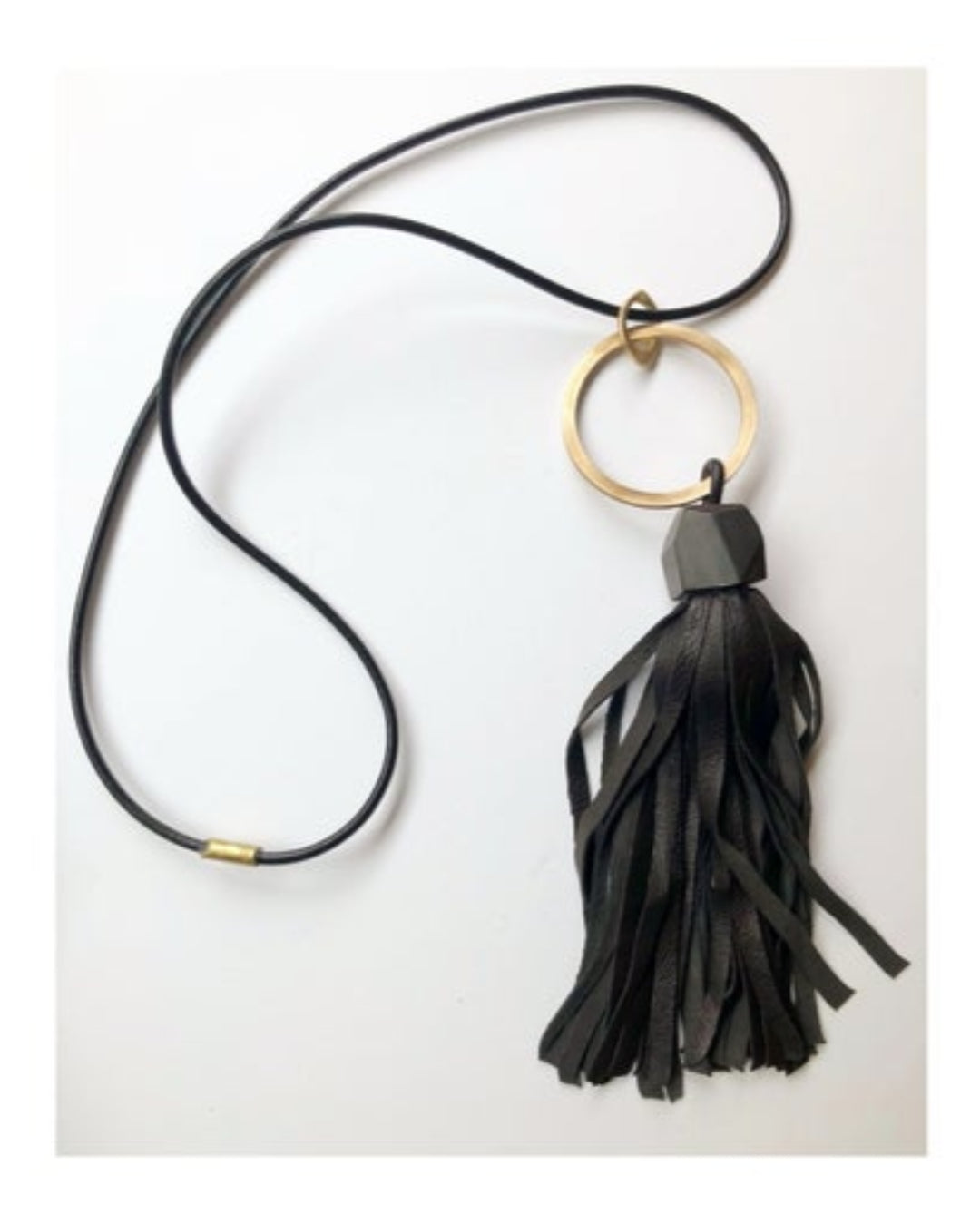 Black leather tassel necklace with a gold ring pendant on a white background