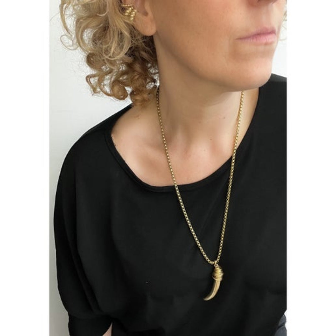 Person wearing a black top and gold necklace with a horn shaped pendant.