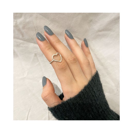 Hand wearing a heart-shaped ring with gray nail polish on a neutral background
