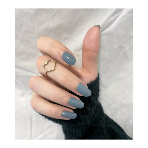 Hand with grey nail polish wearing a gold heart-shaped ring on a white background