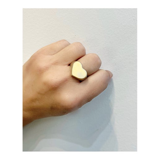 Gold heart-shaped ring on a finger against a light background