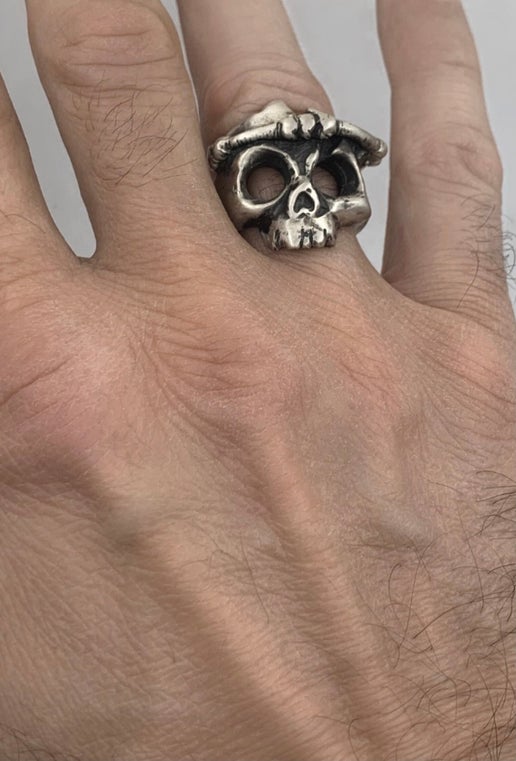 Silver skull ring on a person's finger against a neutral background